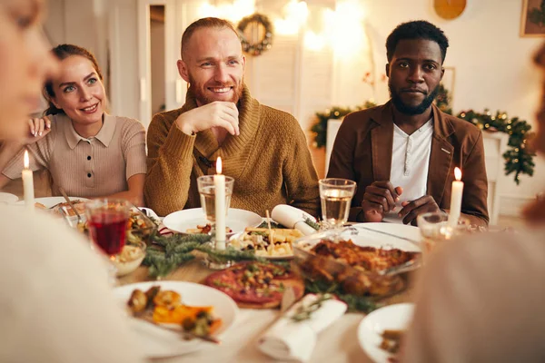 多民族人群坐在餐桌旁享用美味佳肴 以笑容满面的男人为中心的写照 — 图库照片