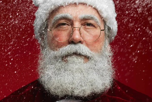 接近童话般圣诞老人的肖像 看着红色背景上飘着雪的相机 — 图库照片