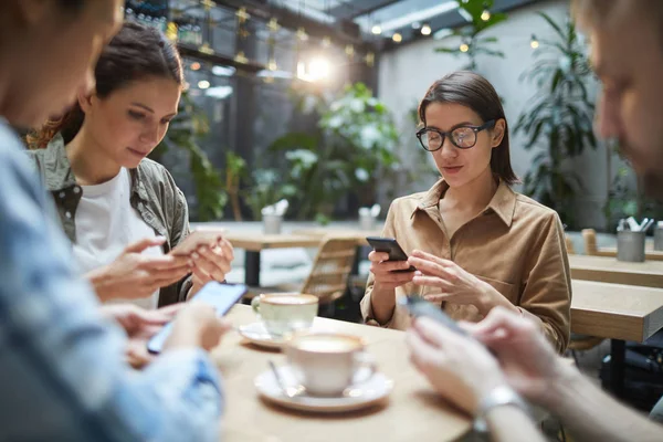 Grupo Jóvenes Sentados Mesa Cafetería Usando Teléfonos Inteligentes Silencio Espacio —  Fotos de Stock