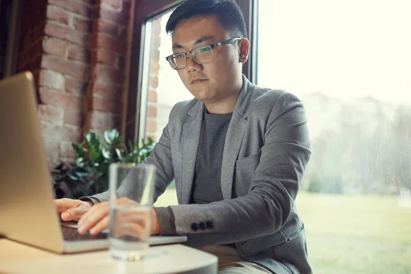 窓辺で仕事をしながらノートパソコンを使っている若いアジア人ビジネスマンの肖像画 コピースペース — ストック写真