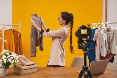 Moda ve güzellik kanalı için video çekerken elinde örgü ören çağdaş genç kadının portresi sarı arka planda, kopyalama alanı