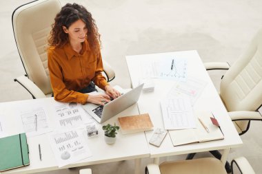 Uzun kıvırcık saçlı zarif bir kadın laptopta yüksek açılı bir şey mesaj atıyor.