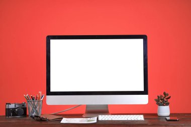Workplace concept with blank white computer screen at wooden desk over coral background, copy space