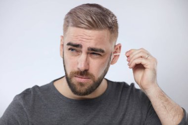 Yatay kafa ve omuzlar. Yüzünde sakal olan genç adamın portresi. Kulağını temizliyor.