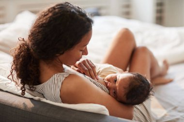 Genç Afro-Amerikan anne portresi. Çocuğu emziriyor. Kameraya bakıyor, boşluğu kopyalıyor.