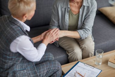 Olgun bir kadının el ele tutuşup terapi seansında onu rahatlatırken ilgilenen kadın psikoloğun yüksek açılı portresi.