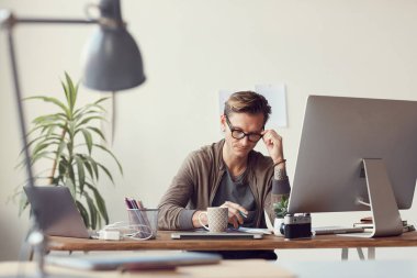 Portrait of contemporary businessman working in office, adjusting glasses and reading documents at wooden desk, copy space