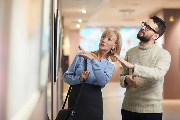 Waist up portrait of modern adult couple looking at paintings while enjoying exhibition in art gallery or museum