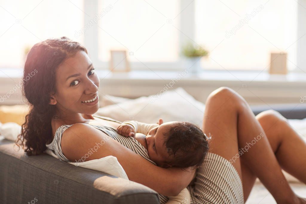 Side view portrait of young African-American mother breastfeeding cute baby boy and looking at camera, copy space