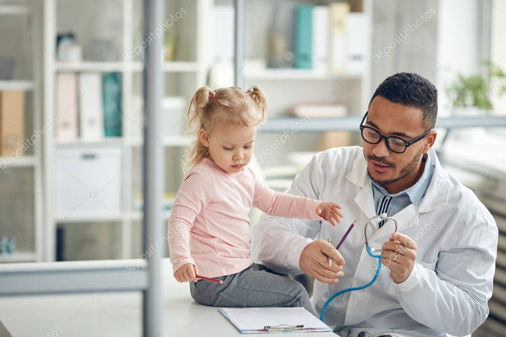 Portrait of African-American doctor examining cute little girl in modern clinic, copy space