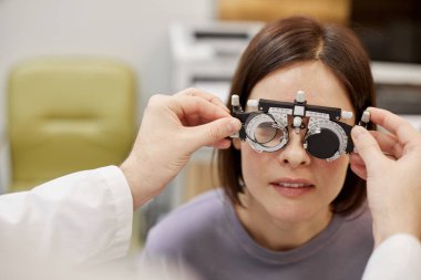 Closeup of unrecognizable ophthalmologist putting trial frame on female patient during vision check in modern clinic, copy space clipart