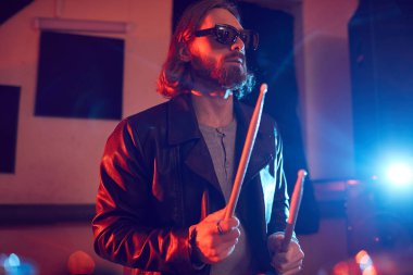 Parlak ışıklarda müzik konserinde davul çalan yakışıklı bir gencin belden yukarı portresi.