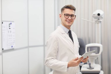 İş yerinde optik ekipmanlarla poz verirken kameraya gülümseyen erkek optometristin belden yukarı portresi, kopyalama alanı
