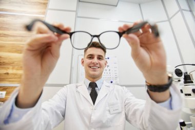 Modern klinikte görüş testi sırasında tanınmayan bir hastaya gözlük takan gülümseyen optometristin POV görüntüsü.