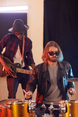 Müzik stüdyosunda prova yapan iki rock grubunun portresi.