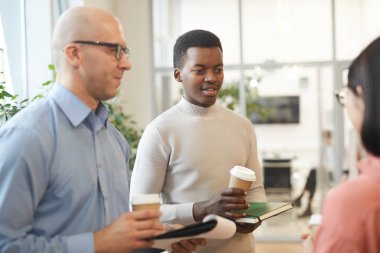 Ofiste dikilen ve elinde kahve fincanı tutan genç Afrikalı adama odaklanan çok ırklı iş adamları.