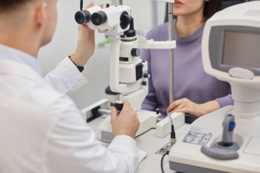 Modern optalmoloji kliniğinde görme testi sırasında makine kullanan genç bir kadının kırpılmış portresi.