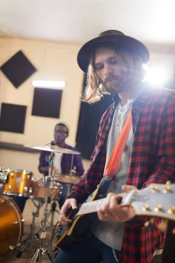 Prova sırasında gitar çalan çağdaş uzun saçlı bir adamın belden yukarı portresi ya da orkestrayla müzik konseri