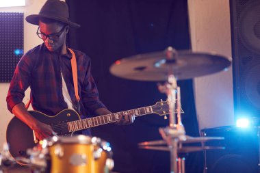 Kayıt stüdyosunda müzik grubuyla birlikte gitar çalan çağdaş Afro-Amerikan bir adamın portresi.