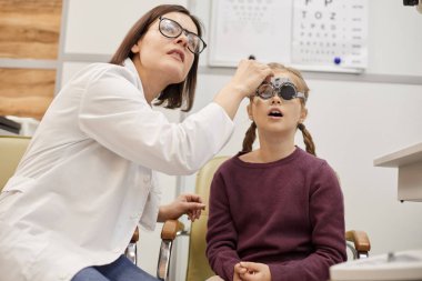 Modern oftalmoloji kliniğinde çocuk görme testi sırasında deneme çerçevesi takan sevimli genç kız portresi