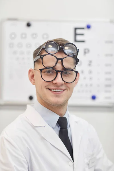 笑顔の若い眼科医の肖像画は 多くの眼鏡を着用しながら オフィスでのビジュアルチャートの横にポーズ スペースをコピー — ストック写真