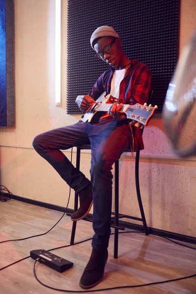 現代アフリカ系アメリカ人男性の完全な長さの肖像は リハーサルやコンサート中に高椅子に座ってギターを演奏薄暗い照明スタジオで — ストック写真