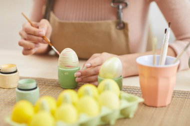 Paskalya için pastel renkte yumurta boyayan genç bir kadının mutfak veya sanat stüdyosunda otururken resmini çek.