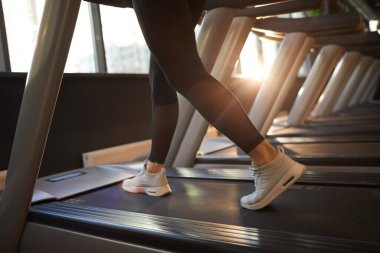 Güneşli spor salonunda koşu bandında koşan sportif genç kadının düşük kesimli portresi.