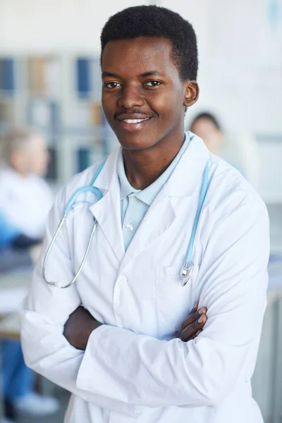 Waist up portrait of young African-American doctor standing with arms crossed and smiling at camera against medical conference background