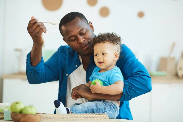 Retrato Papá Afroamericano Feliz Alimentando Lindo Niño Sentado Mesa Cocina —  Fotos de Stock