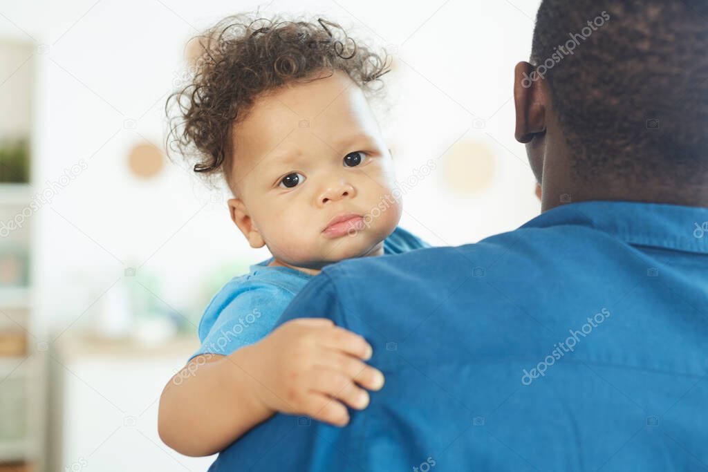 Portrait of cute African-American baby looking at camera while sitting in fathers arms, copy space
