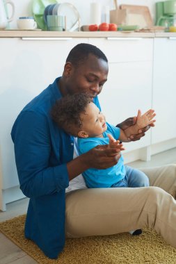 Küçük çocukla oynayan mutlu Afro-Amerikan babasının dikey portresi, evde oturmuş, boşluğu kopyalıyor.