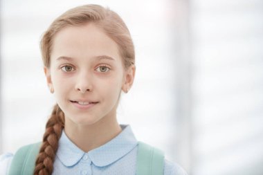 Sırt çantası takan ve kameraya gülümseyen sarışın kızın kafa ve omuz portresi.