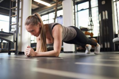 Modern spor salonunda egzersiz yapan sportif genç bir kadının tam boy portresi.