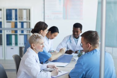Tıbbi konsey veya klinikteki konferans sırasında yuvarlak masa başında oturan bir grup doktora yan bakış, kopyalama alanı