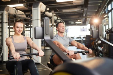 Modern spor salonunda egzersiz yaparken egzersiz makineleri kullanan gülümseyen sporcu çiftin portresi.
