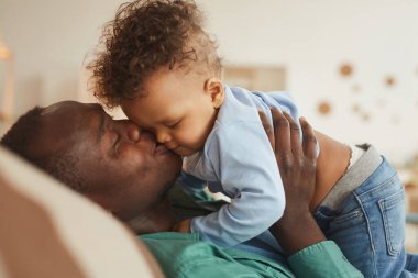 Afro-Amerikan bir babanın evde oynarken oğlunu öpmesi, fotokopi çekmesi.