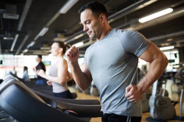 Modern spor salonunda koşu bandında koşan olgun kaslı bir adamın yan görünüş portresi.