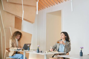 İki genç kadının geniş açılı portresi iş hayatında gelişigüzel çalışması ya da kapalı bir kafede ayrı masalarda oturması, kopyalama alanı.