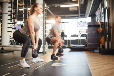 Modern spor salonunda ağırlık çalışırken sallayan kaslı çiftin tam boy yan görünüm portresi.