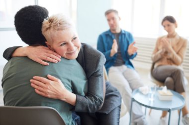 Destek grubunda Afrikalı-Amerikalı gençleri kucaklayan gülümseyen kadın psikoloğun portresi.