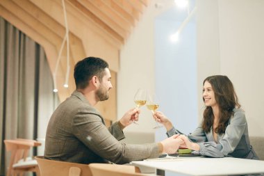 Kafede buluşmanın keyfini çıkarırken şampanya bardaklarını tokuşturan modern çiftin minimal yan görünüm portresi.