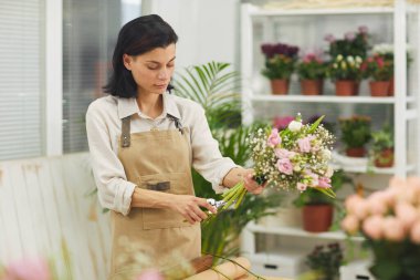 Güzel çiçekçi dükkanında çalışırken, çiçek buketi düzenleyen modern kadın çiçekçinin belden yukarı portresi.