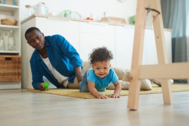 Evde babamla oynarken halıda sürünen tatlı Afro-Amerikan bebek portresi.