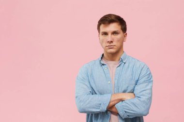 Kolları çapraz duran ve stüdyoda pembe arka planda poz verirken kameraya bakan yetişkin bir adamın belden yukarı portresi.