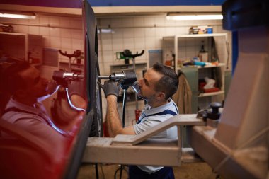 Oto tamir atölyesinde kırmızı lüks arabanın tekerleklerini değiştiren olgun araba tamircisinin yan görünüm portresi, boşluğu kopyala