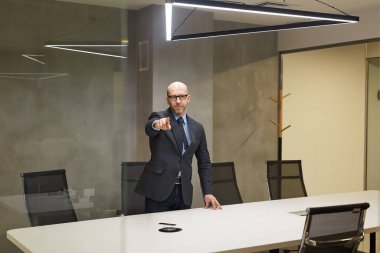 Cam duvarın arkasındaki konferans masasında duran başarılı kel iş adamının geniş açılı portresi.