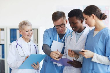 Tıp bürosunun içinde dururken ellerinde pano tutan çok ırklı bir sağlık ekibi.