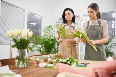 Çiçek kompozisyonları düzenleyen ve dükkanda çalışırken bahar laleleriyle buketleri düzenleyen iki kadın çiçekçinin belden yukarı portresi