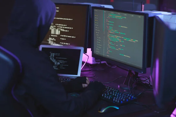 暗室でプログラミングコードの作業中にフードを身に着けている認識できないサイバーセキュリティハッカーのバックビュー コピースペース — ストック写真